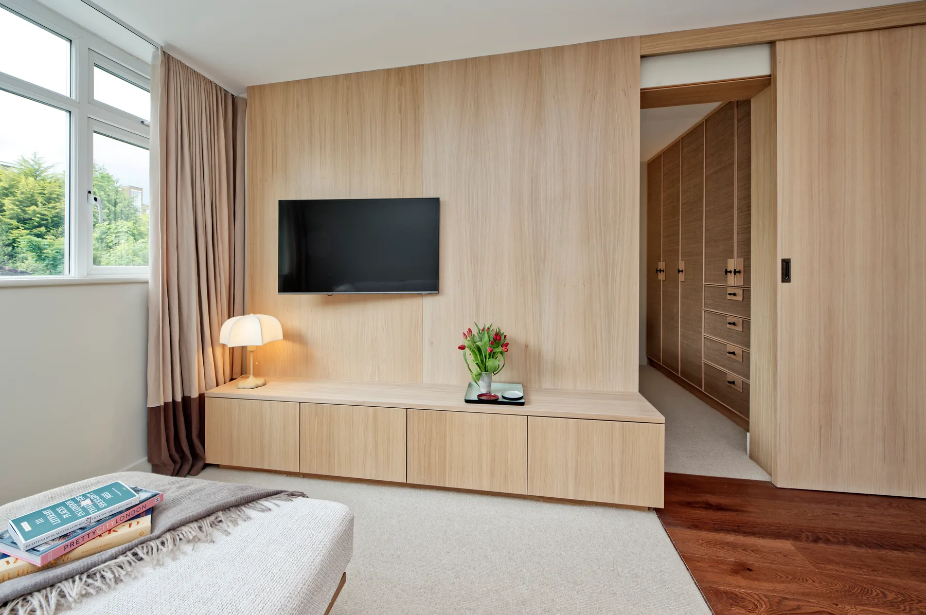 A bedroom seating area with a wall-mounted television and large windows.