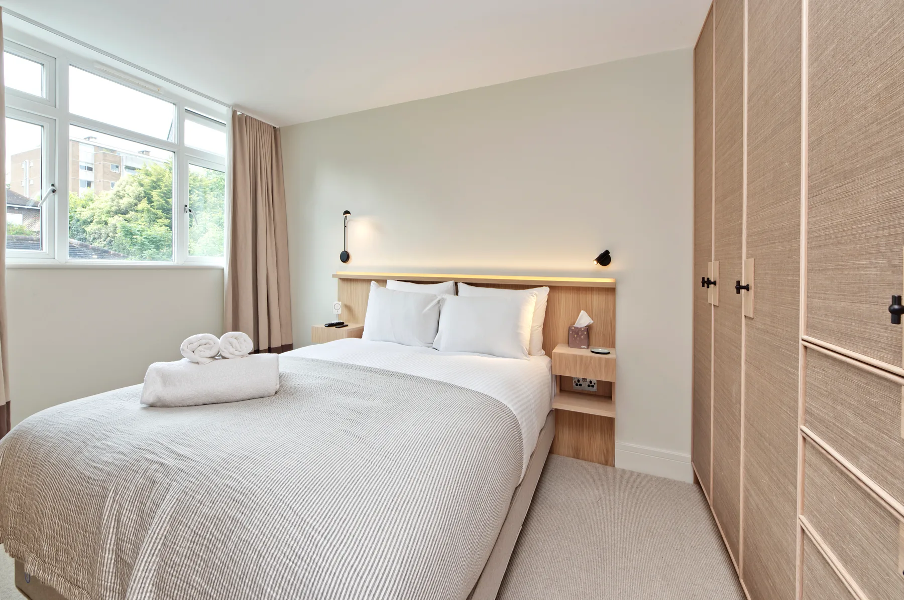 A bright bedroom with a neatly made bed beside a large window.