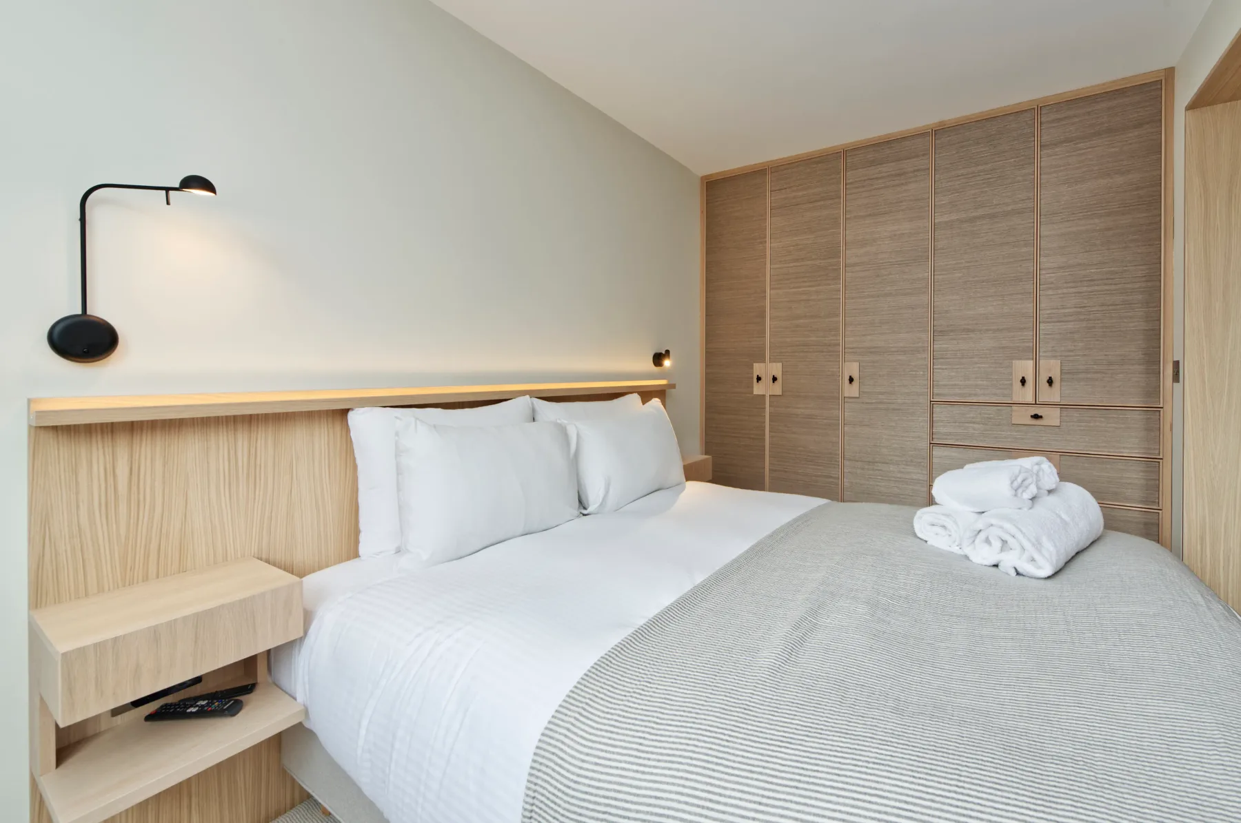 A bedroom with a neatly made bed and built-in wood cabinetry.
