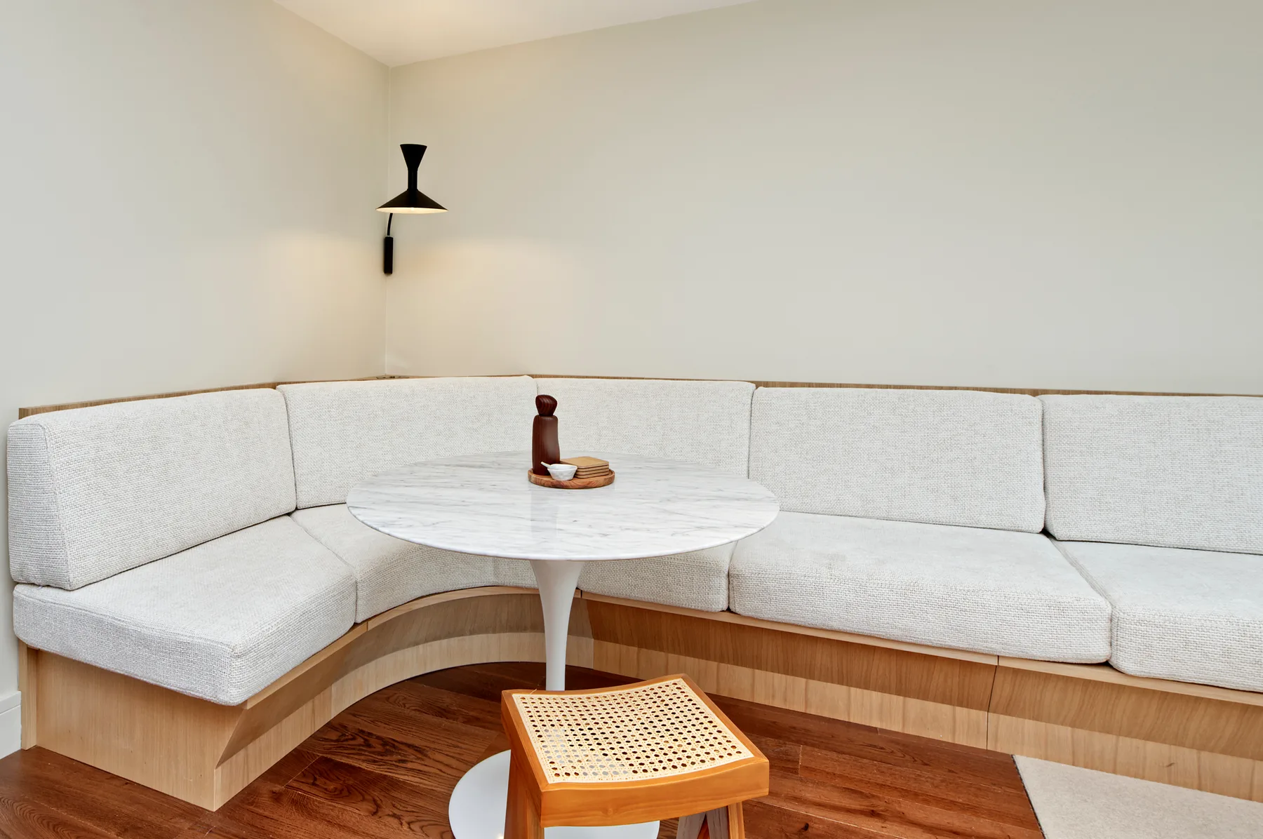 A curved cushioned seating nook surrounds a round table in a bright room.