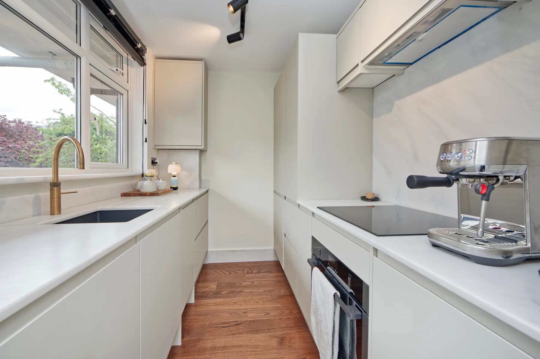 A bright modern kitchen with a long counter, windows, and a coffee machine.