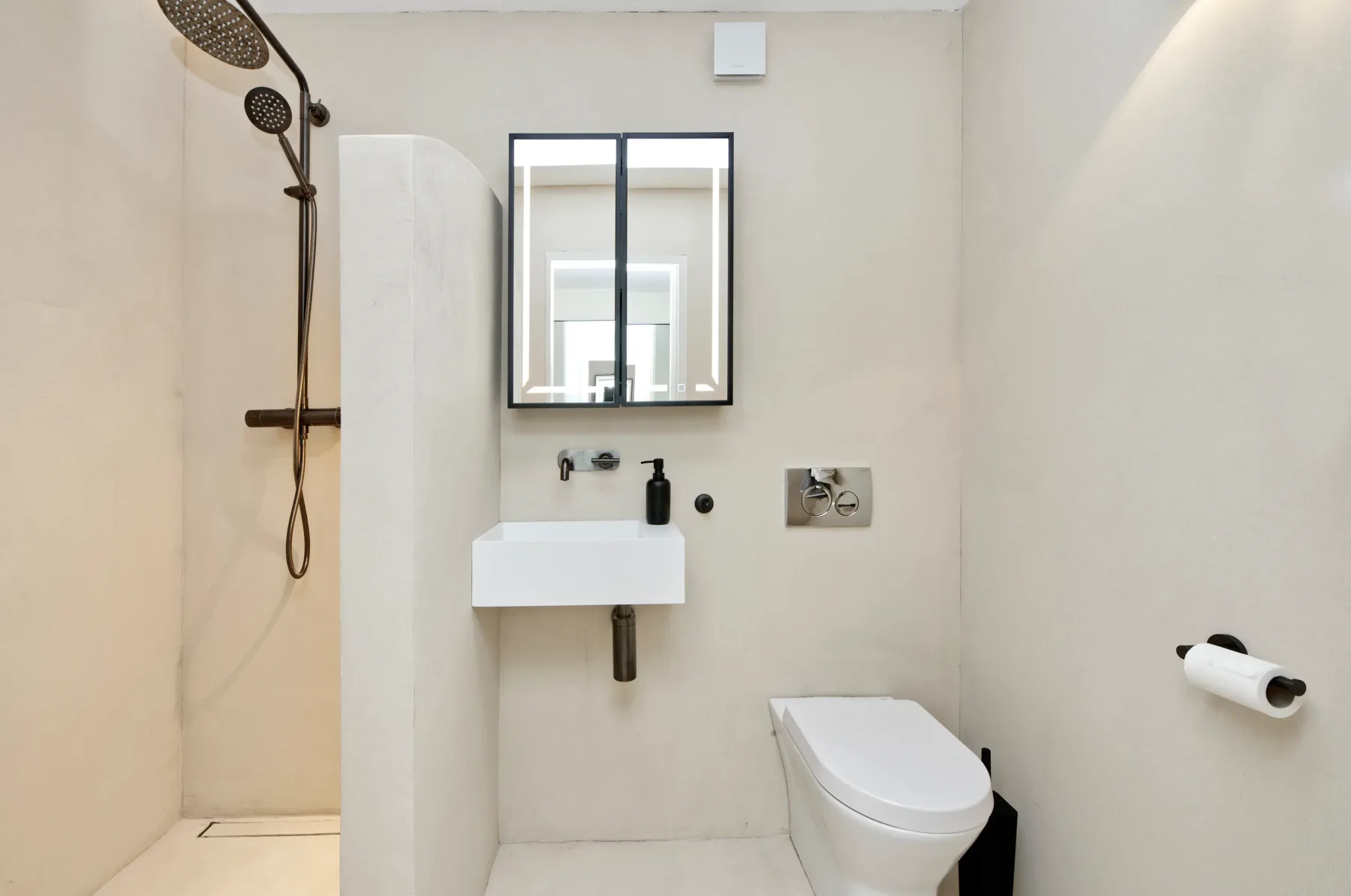 A bathroom with a wall-mounted sink, mirror, shower, and toilet.