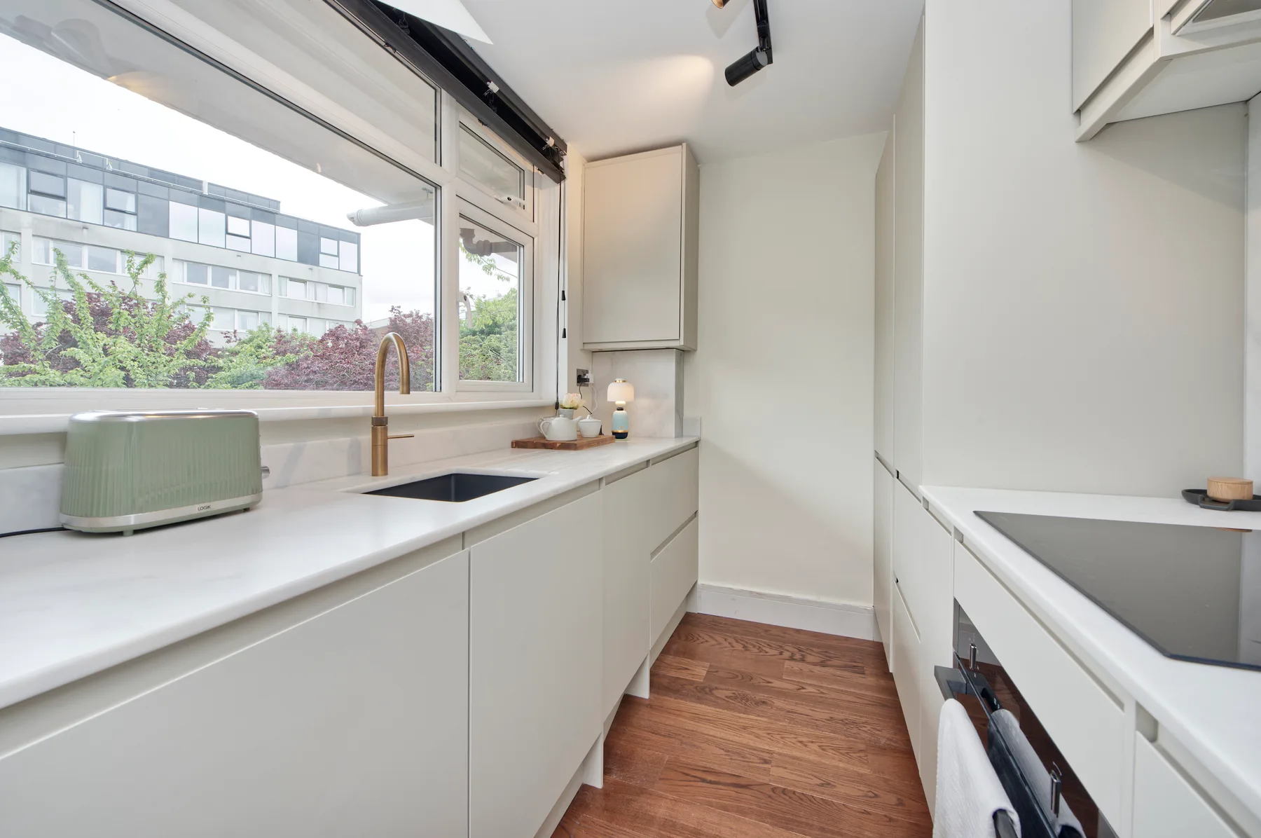 A bright kitchen with white counters, a window, and wood flooring.