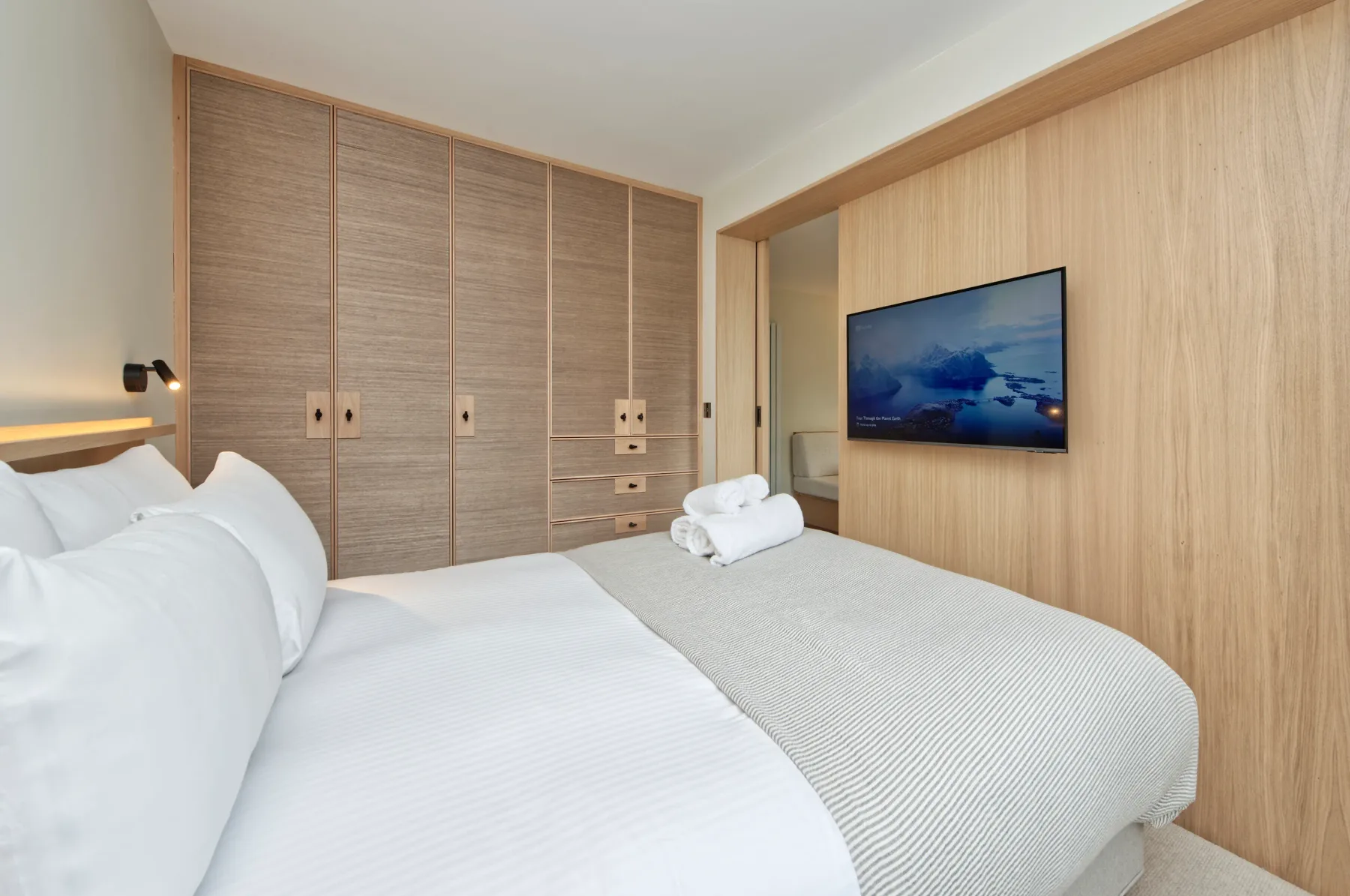 A bedroom with white bedding, built-in storage, and a wall-mounted television.