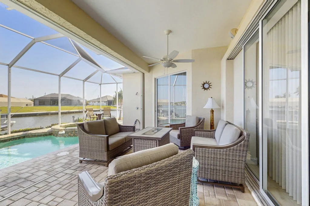 A screened patio with wicker seating overlooks a swimming pool and canal.