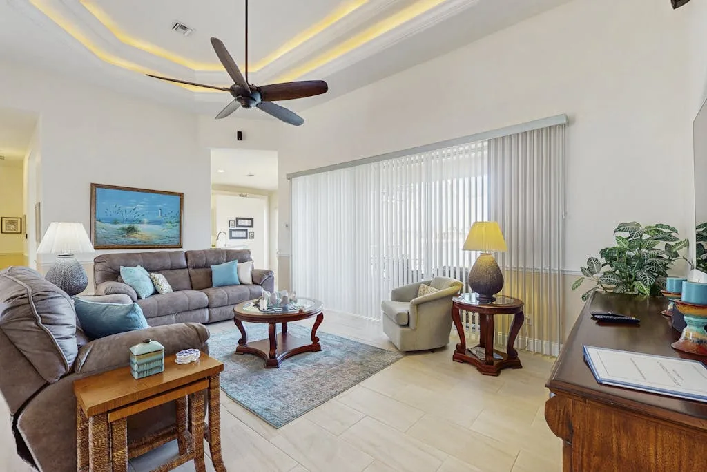 A bright living room with seating, a coffee table, and large curtained windows.