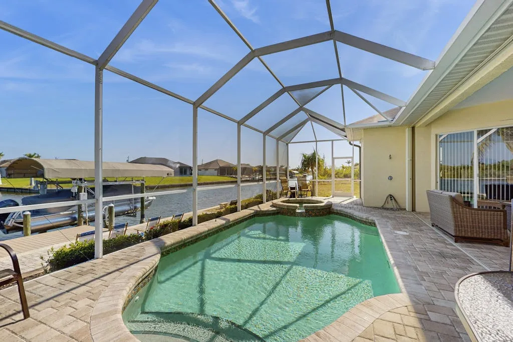A screened outdoor pool beside a paved patio, with a canal visible beyond.