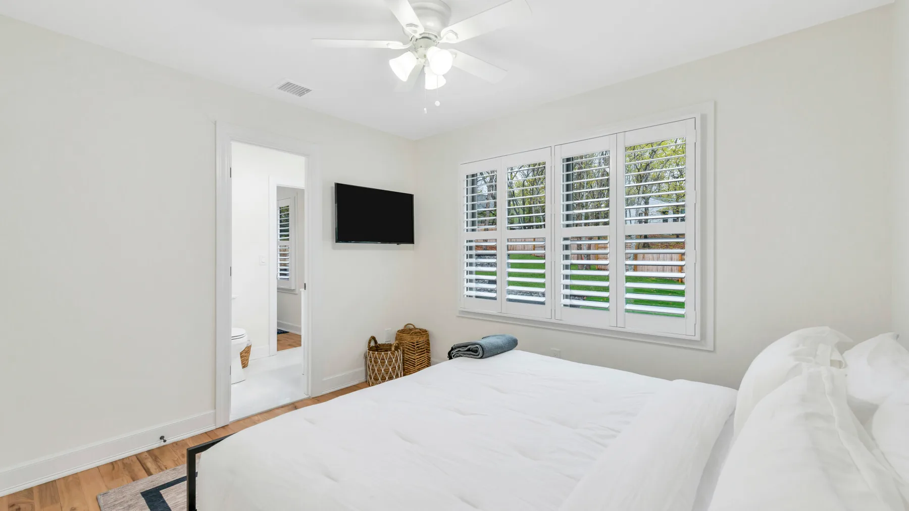 Un dormitorio luminoso con una cama grande, ventanas con persianas y un ventilador de techo.