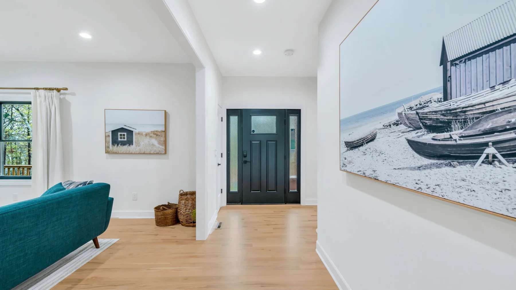A bright living room opens toward a dark front door, with teal seating and framed artwork.