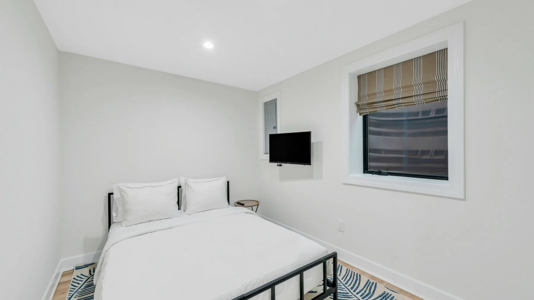 Un dormitorio luminoso con una cama tendida y una ventana con persianas.