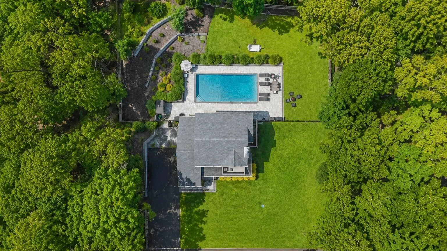Una vista aérea muestra una casa, una piscina y un césped rodeados de árboles.