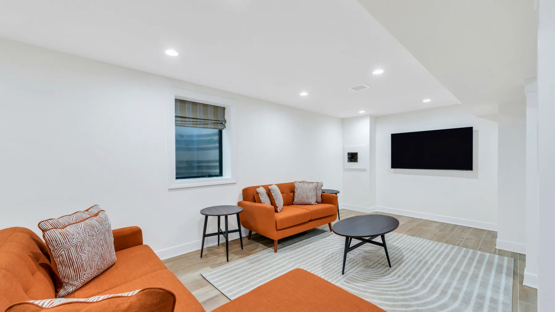 Una sala luminosa con asientos naranjas, una mesa de centro y un televisor en la pared.