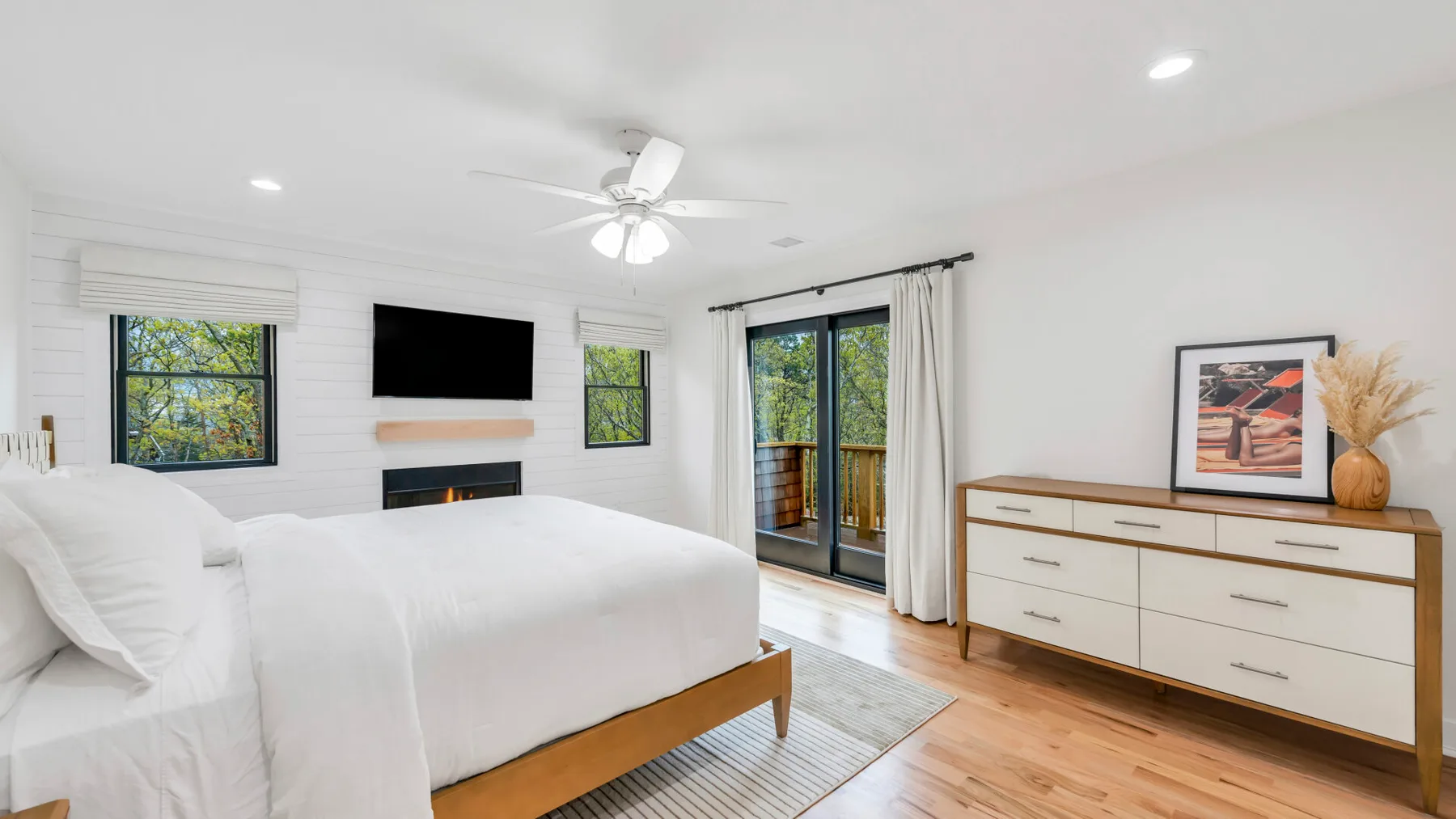 Un dormitorio luminoso con una cama grande, un televisor en la pared y puertas corredizas de vidrio.