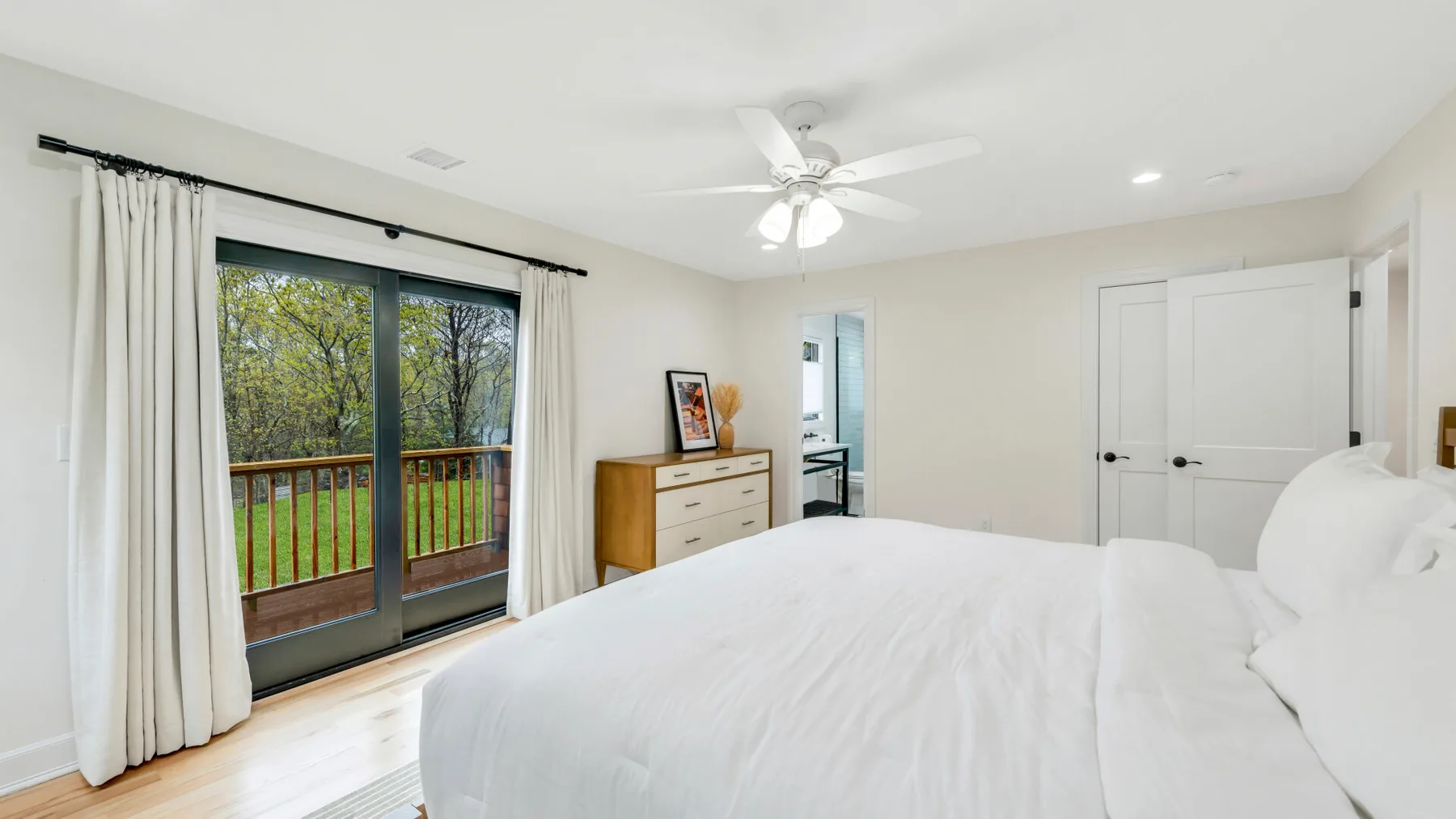 Un dormitorio luminoso con una cama blanca y puertas corredizas de vidrio que dan a un balcón.