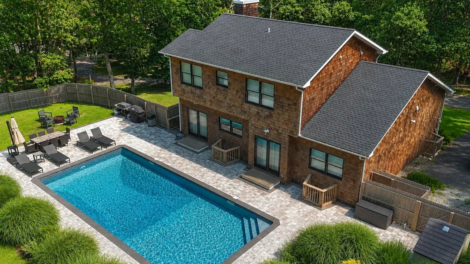 Vista aérea de una casa de dos pisos junto a una piscina y un patio pavimentado.
