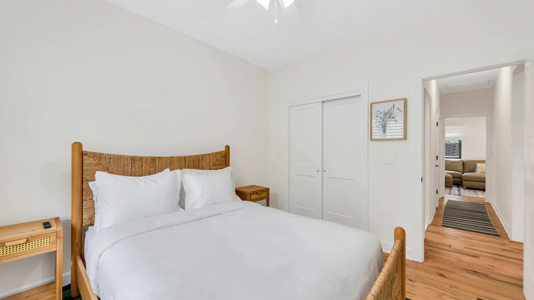 Un dormitorio con una cama blanca, mesitas de noche y vista a través de la puerta.