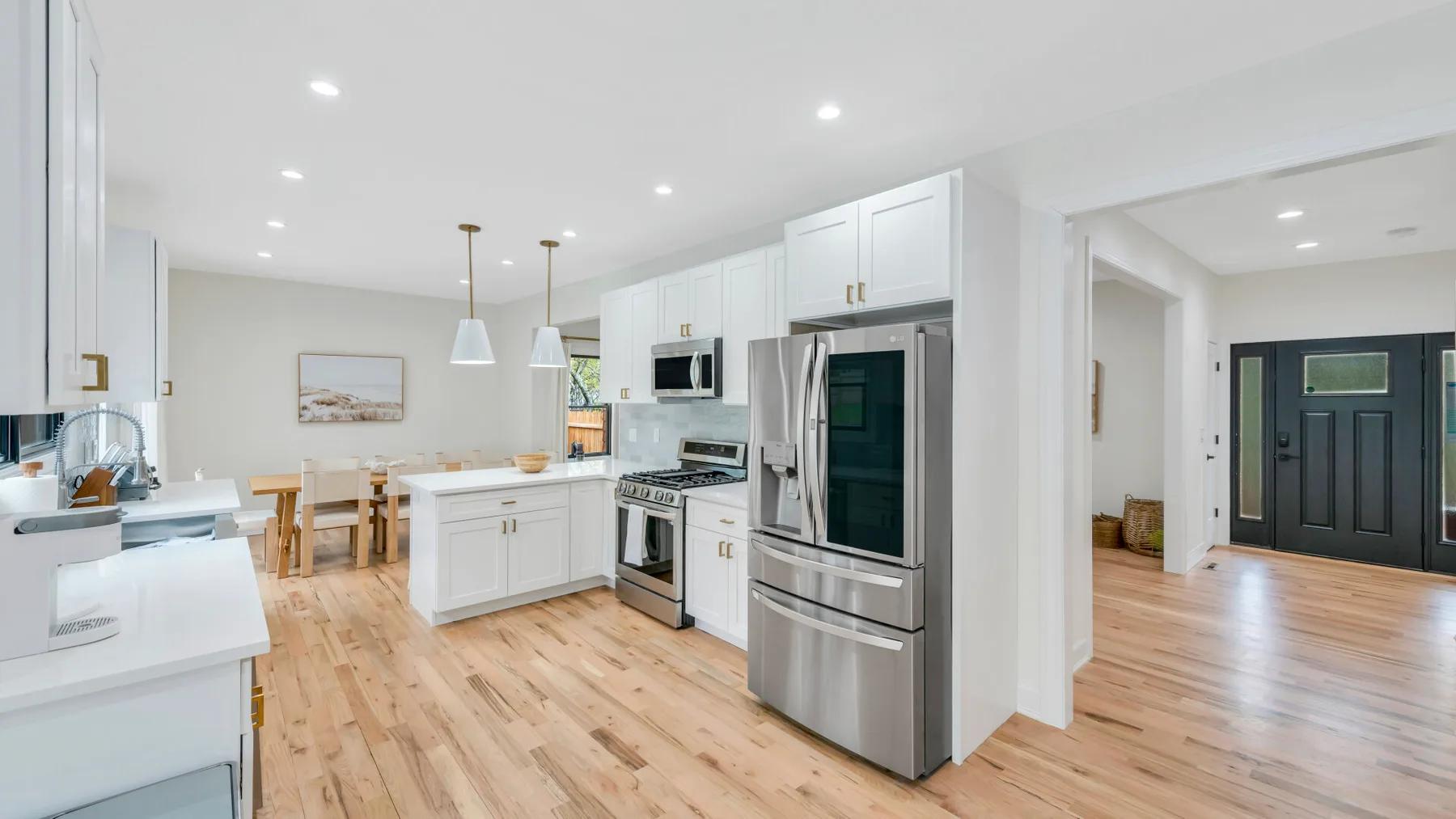 Una cocina luminosa y abierta con gabinetes blancos, electrodomésticos de acero inoxidable y comedor con piso de madera.
