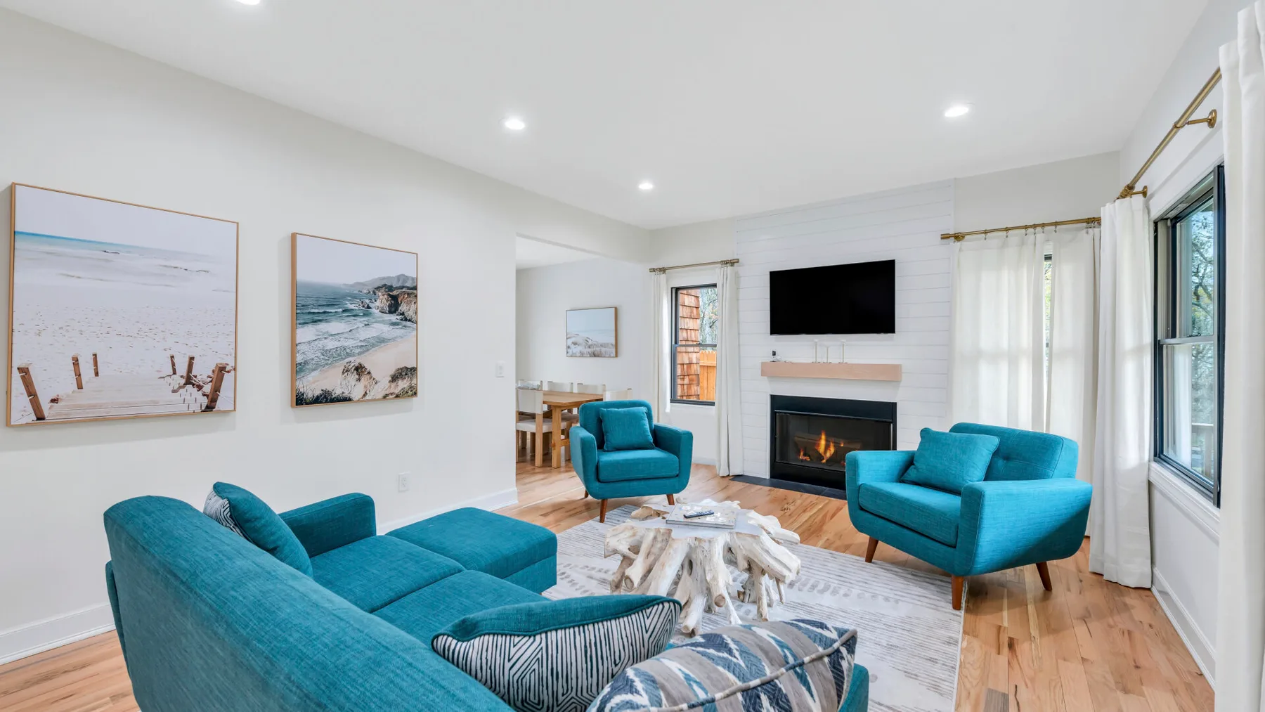 A bright living room with teal seating, a fireplace, and framed beach prints.