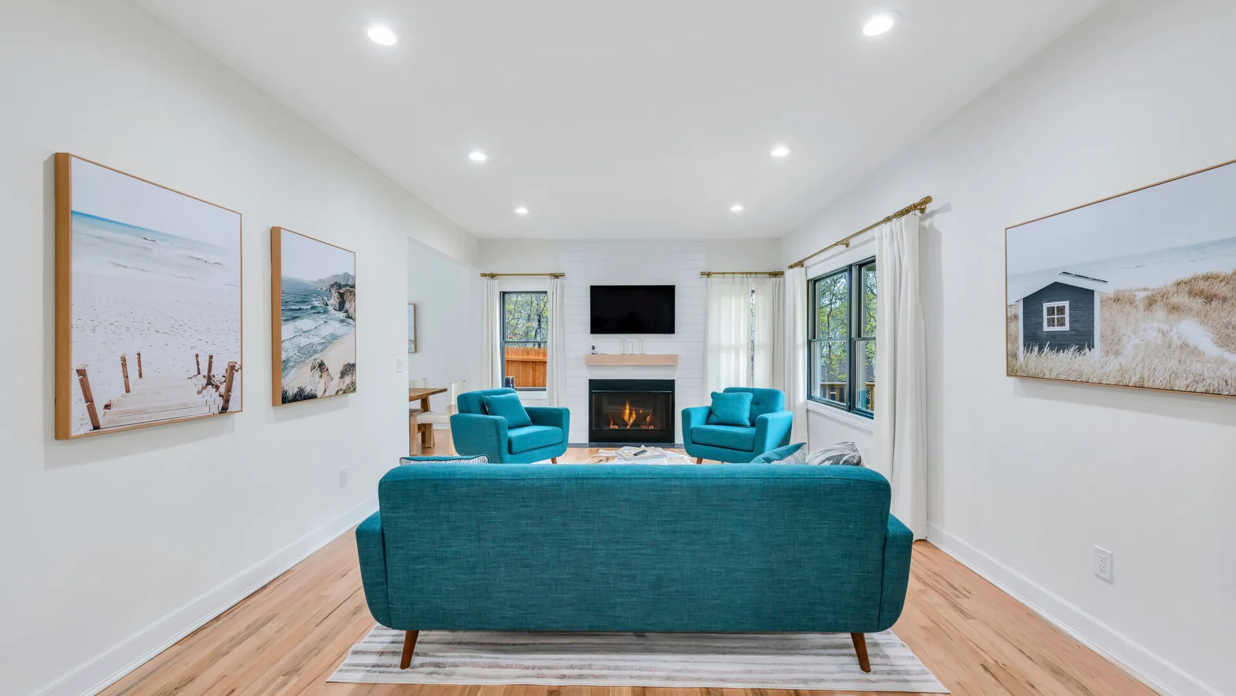 Una sala luminosa con asientos color turquesa, una chimenea y cuadros costeros.
