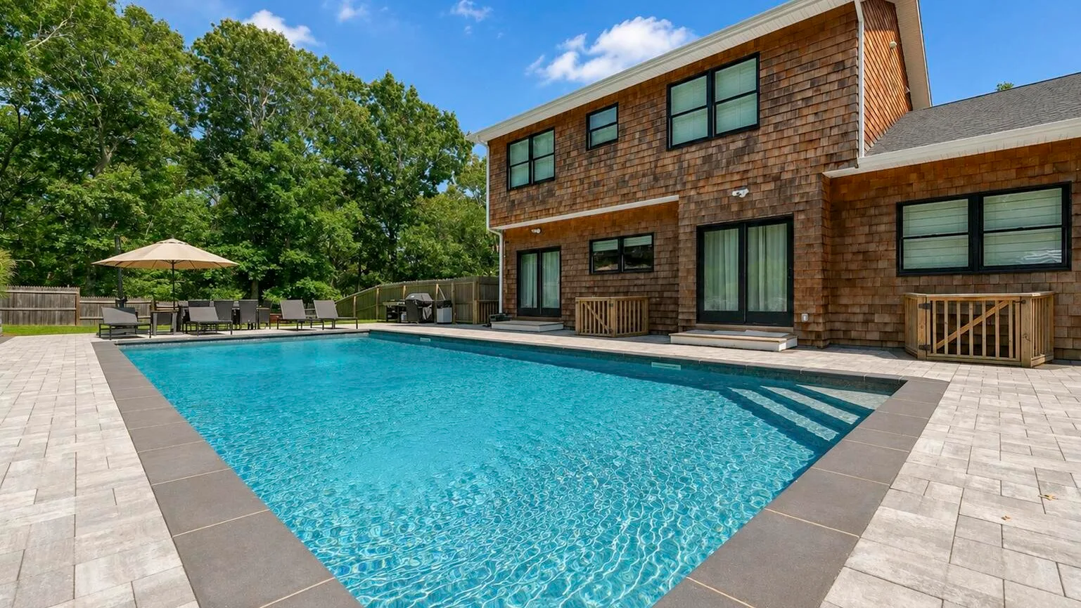 Una piscina exterior junto a una casa de ladrillo y un patio pavimentado.