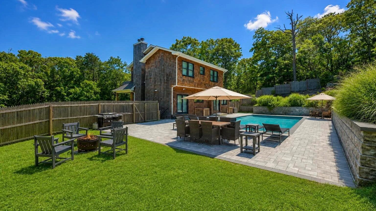 A backyard patio with outdoor seating, umbrellas, and a swimming pool.
