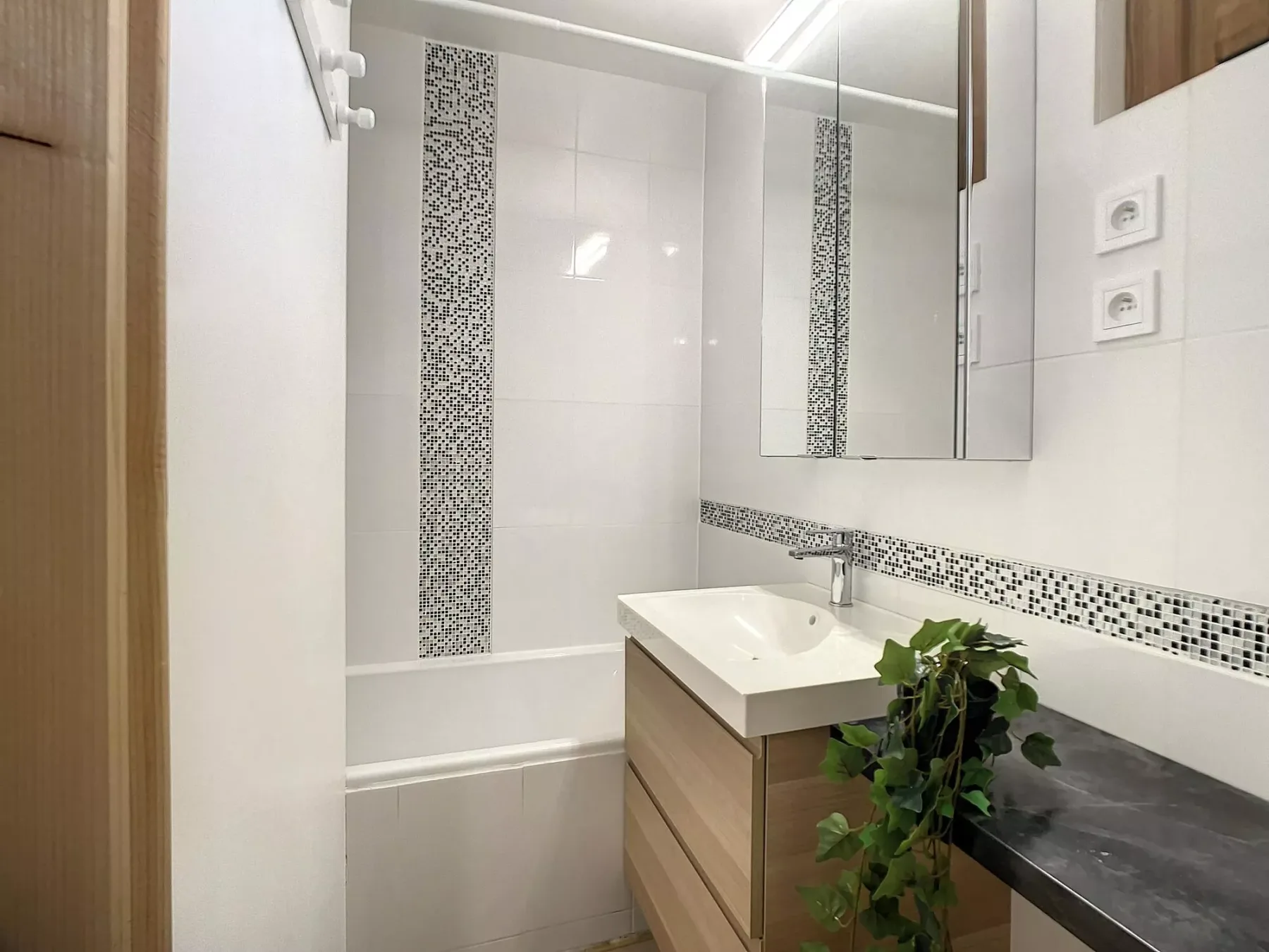 A bright bathroom with a white sink, mirror, and bathtub.