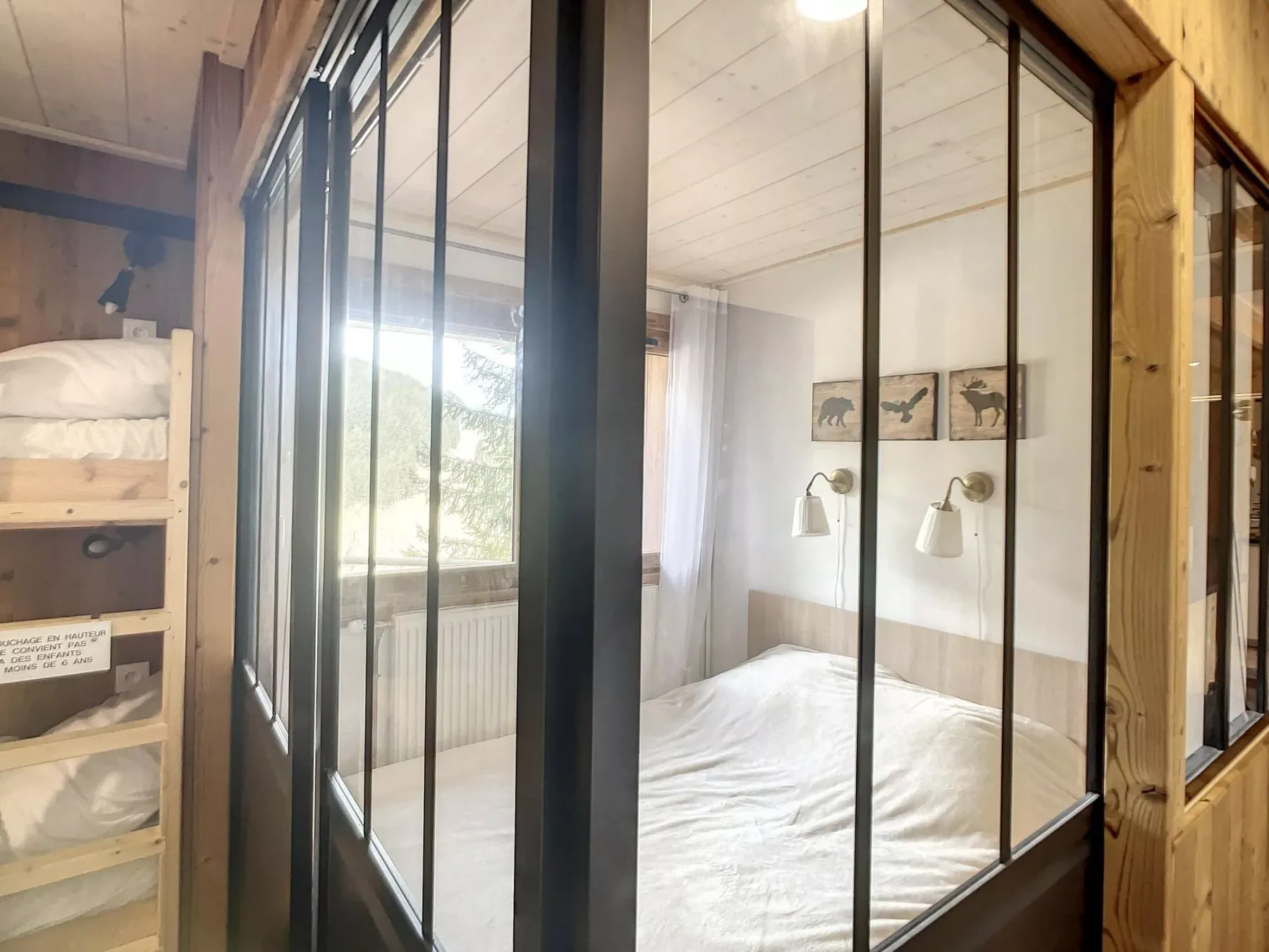 Bedroom with a bed beside a large window and a wooden bunk bed.
