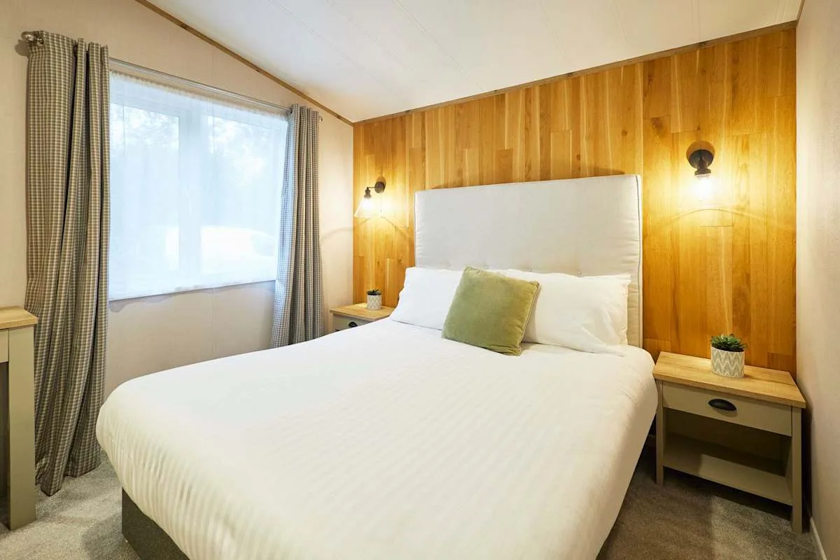 Dormitorio con una cama junto a una pared revestida de madera y una ventana con cortinas.