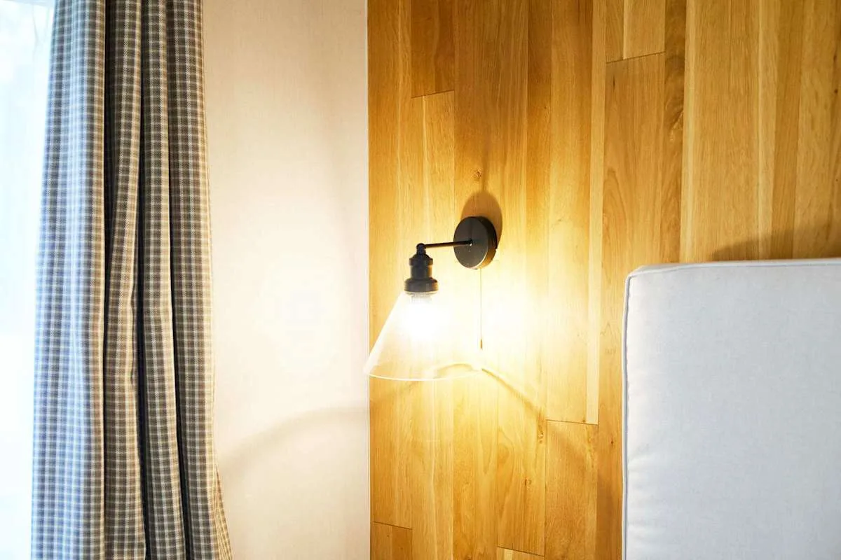 Una lámpara de pared ilumina un panel de madera junto a una cortina.
