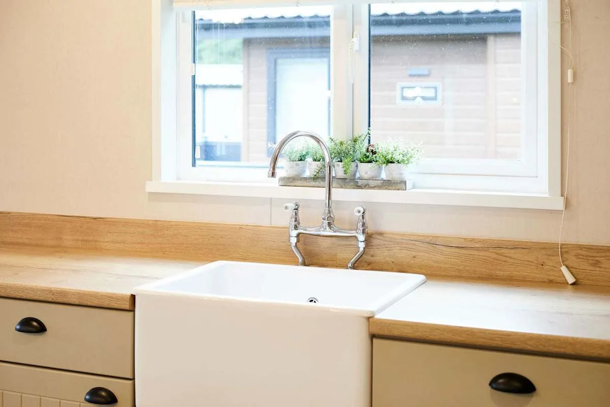 Un fregadero de cocina está bajo una ventana con pequeñas plantas en macetas.