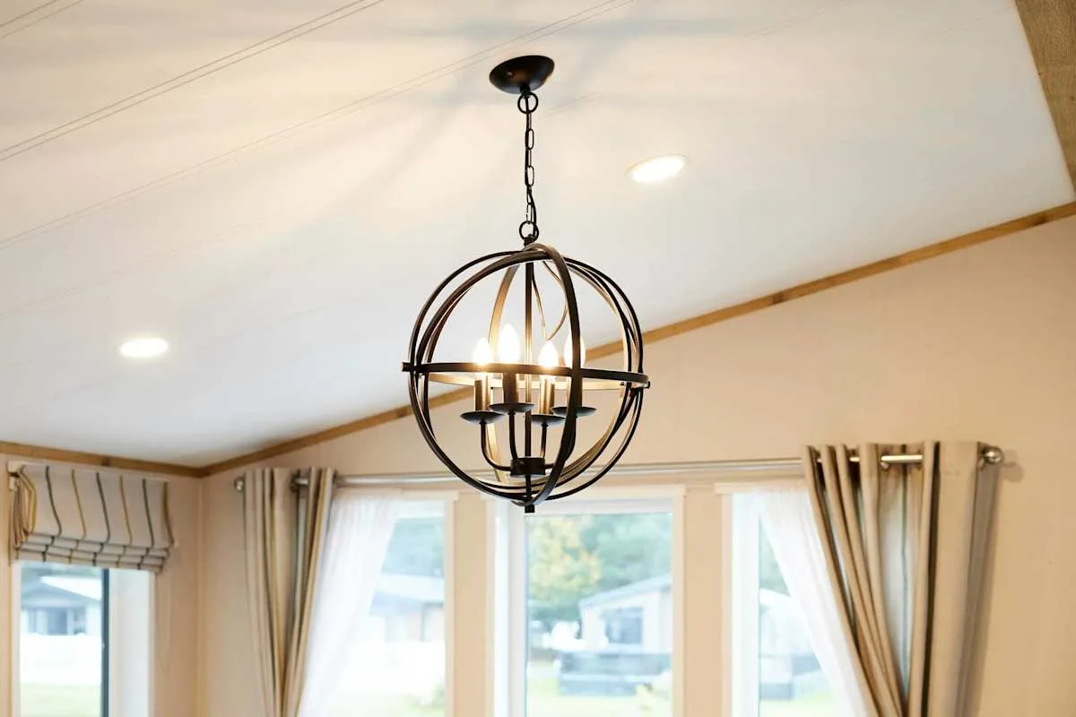 Una habitación luminosa con una lámpara colgante de metal sobre grandes ventanas.