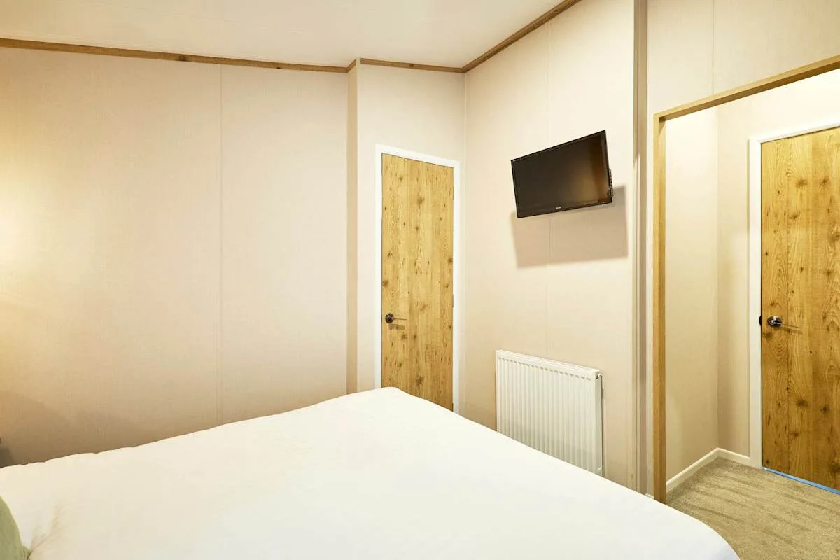 Un dormitorio con una cama, puertas de madera y un televisor en la pared.