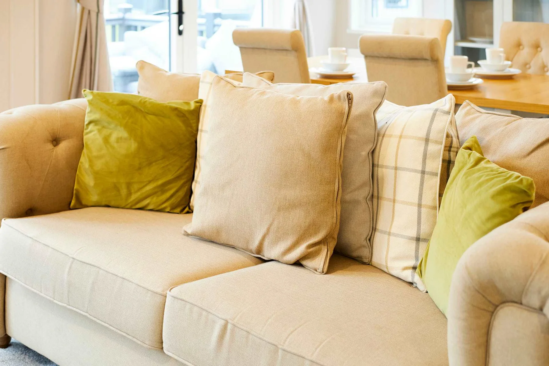 Una sala luminosa con un sofá beige y cojines decorativos verdes.