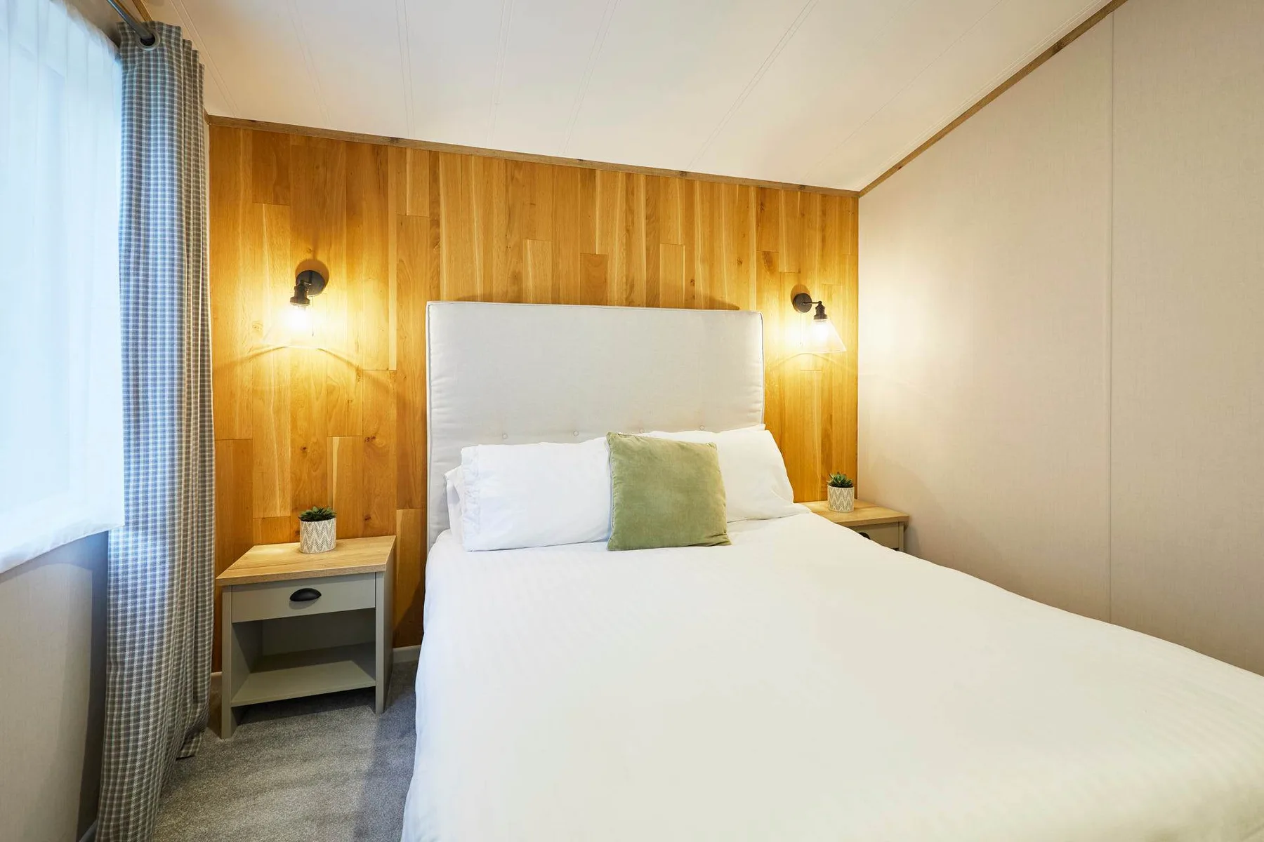 A bedroom with a neatly made bed against a wood-paneled wall.