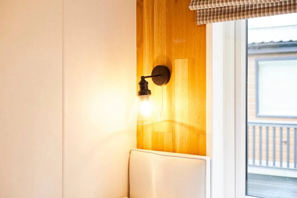 Una pared de dormitorio con un aplique encendido junto a una ventana.