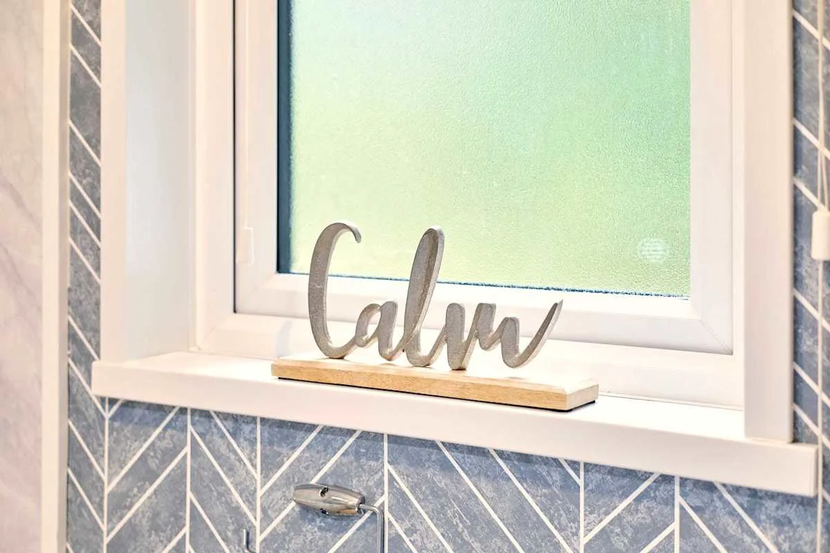 Una ventana de baño con un letrero decorativo que dice «Calm» en el alféizar.