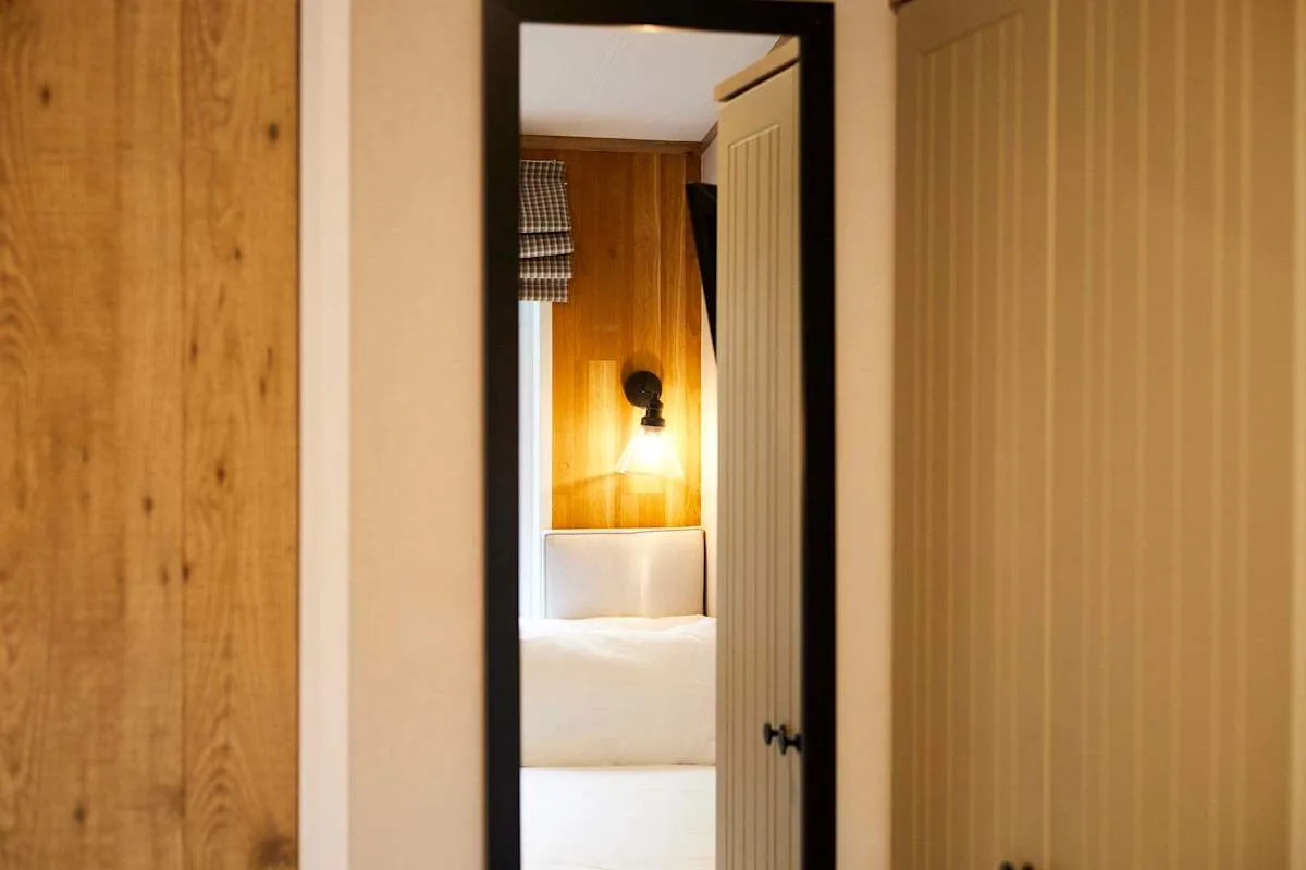 Se ve un dormitorio a través de una puerta abierta, con una cama y una luz de pared.