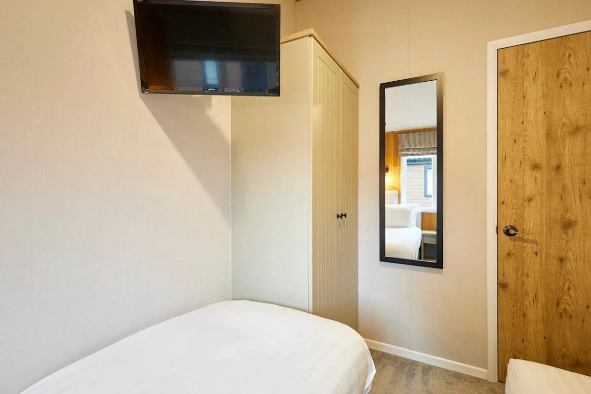 Un dormitorio con cama, televisor de pared, armario y espejo de cuerpo entero.