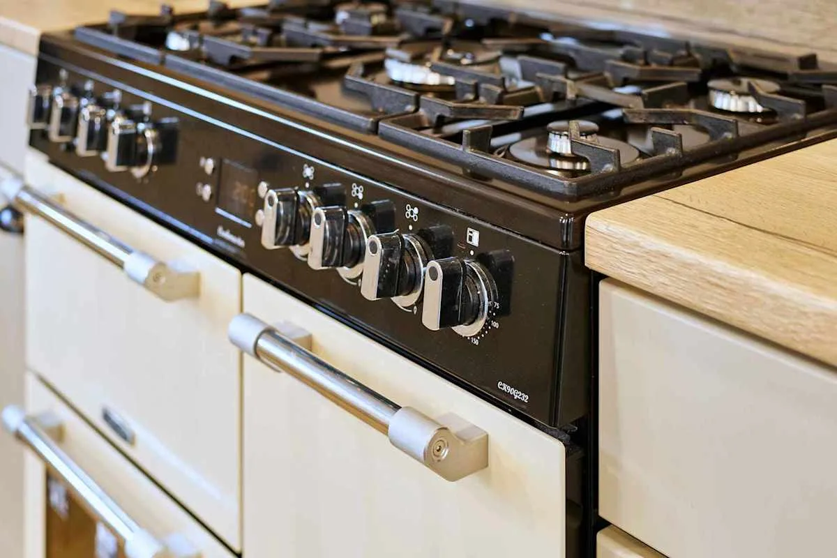 Una estufa de cocina con varios quemadores y perillas está sobre gabinetes claros.