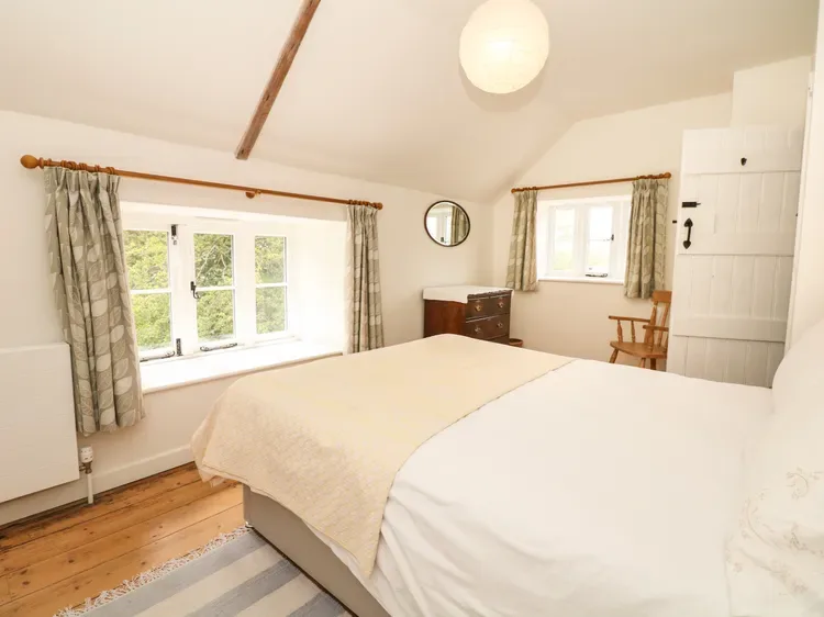 Un dormitorio luminoso con una cama grande, ventanas con cortinas y suelo de madera.