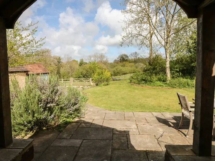 A stone patio opens onto a grassy garden bordered by trees and shrubs.