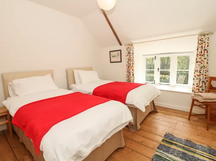 Dormitorio con dos camas vestidas de blanco y rojo, junto a una ventana.