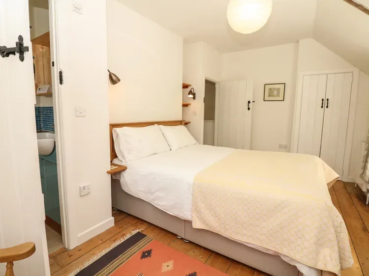 Un dormitorio con una cama, ropa de cama blanca y suelo de madera.