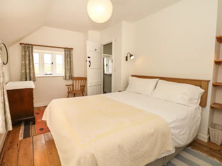 Un dormitorio con una cama, suelo de madera y una ventana con cortinas.