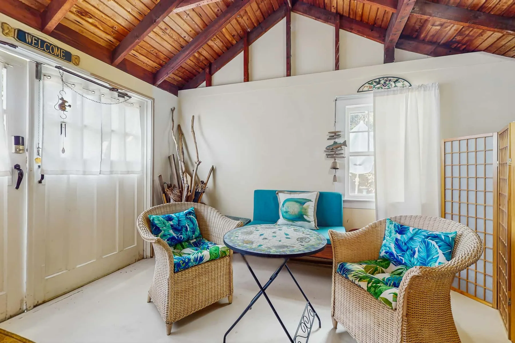 A bright sitting area with wicker seating, a round table, and a wood-beamed ceiling.