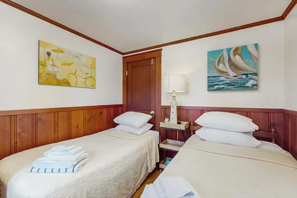 A bedroom with two beds, a bedside table, and nautical wall art.