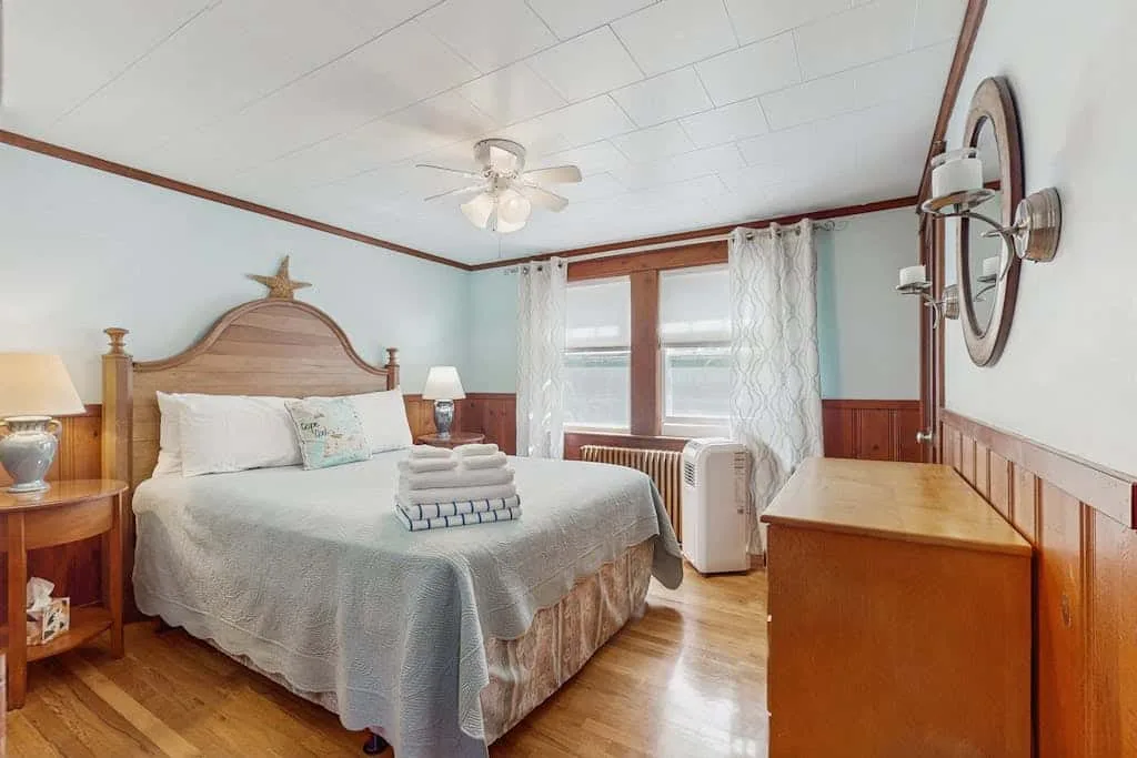 A bedroom with a bed, a ceiling fan, and windows with sheer curtains.