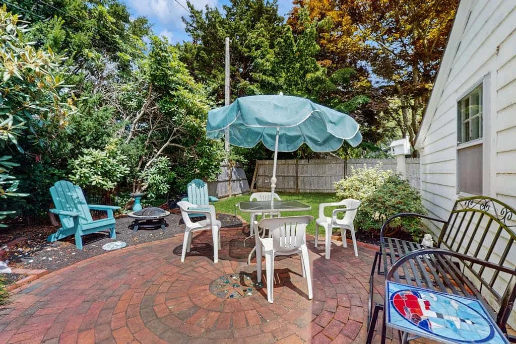 A brick patio with outdoor seating and a large umbrella beside a white house.