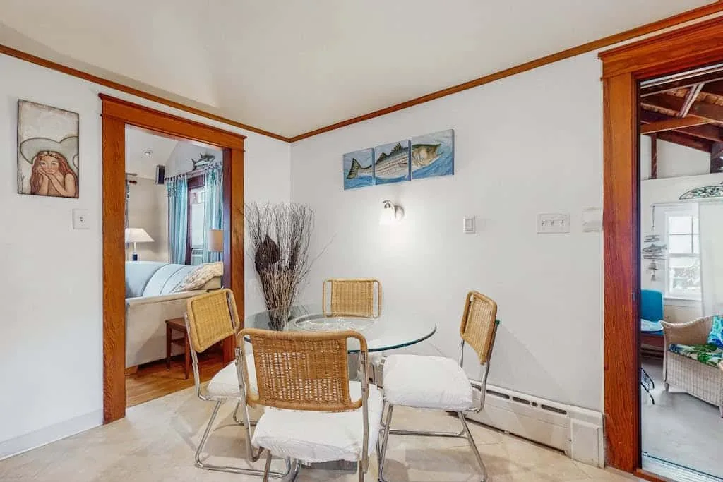 A dining area with a glass table and woven chairs beside open doorways.
