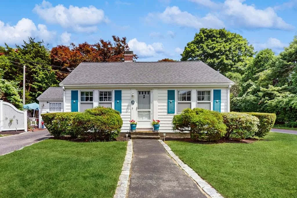 A single-story house with light siding, blue shutters, and a front walkway.